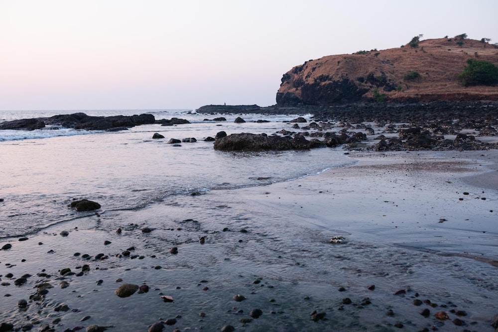 a beach with rocks and water and a hill in the background