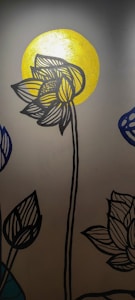 A stylized black outline of a lotus flower with detailed line patterns is depicted against a bright, golden circular background, resembling a sun. Additional lotus blossoms are partially visible on the sides, drawn in a similar style with one in blue.