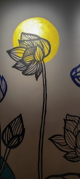 A stylized black outline of a lotus flower with detailed line patterns is depicted against a bright, golden circular background, resembling a sun. Additional lotus blossoms are partially visible on the sides, drawn in a similar style with one in blue.