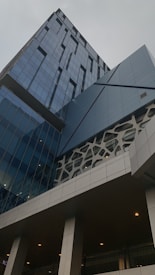 A modern building with an architectural design featuring angular and geometric patterns. The facade is mostly glass, with sections of intricate lattice work. The structure has a sleek, contemporary appearance, and the reflection on the glass gives a dynamic look.