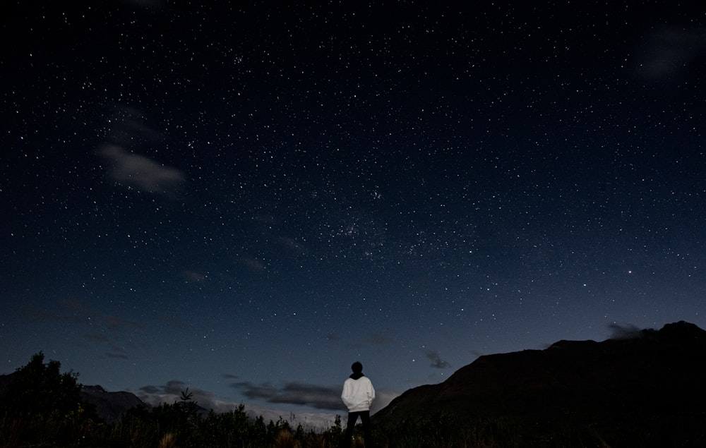 a man standing on top of a lush green hillside under a night sky