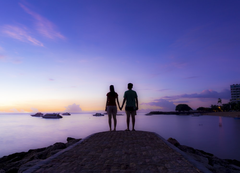 two people standing on a pier looking out at the water