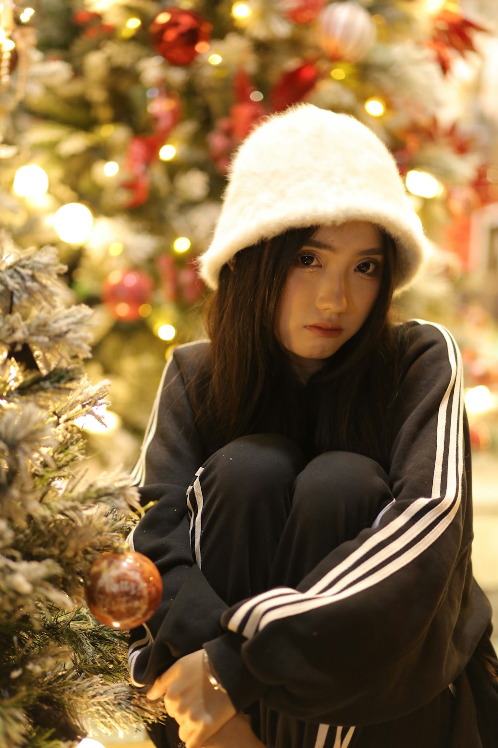 a woman sitting on the ground next to a christmas tree