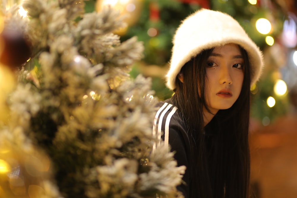 a woman wearing a white hat next to a christmas tree