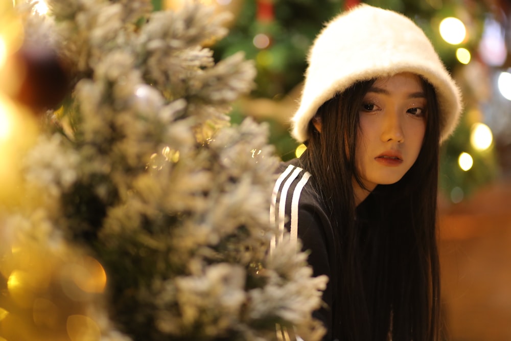 a young woman wearing a white hat next to a christmas tree