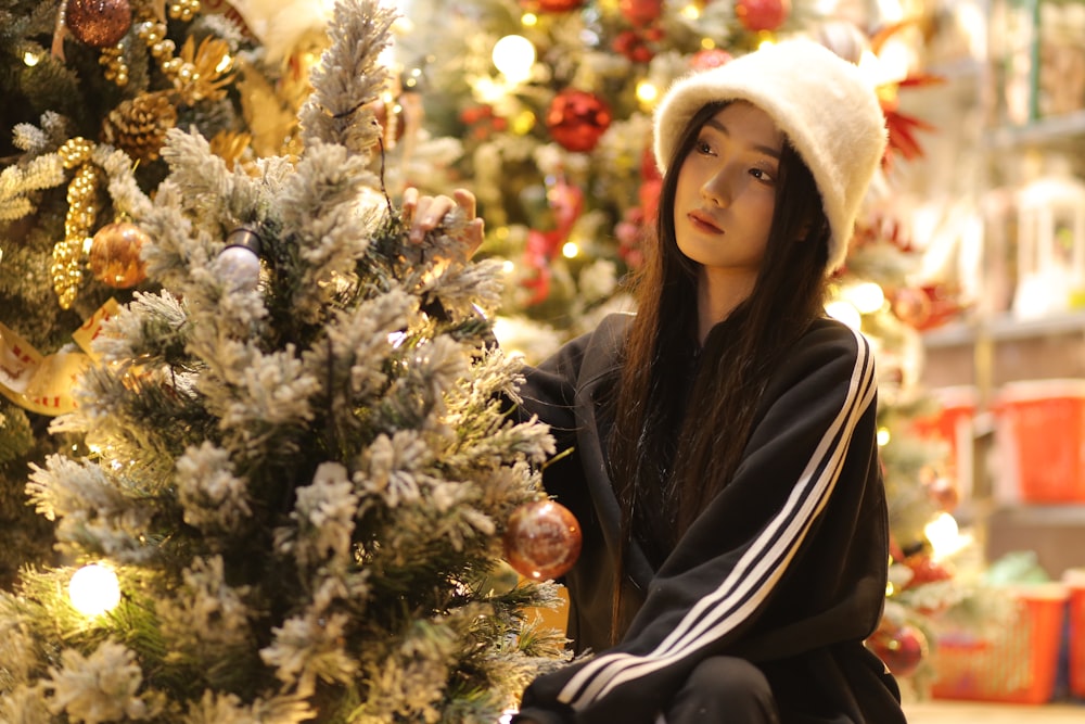 a young girl sitting next to a christmas tree