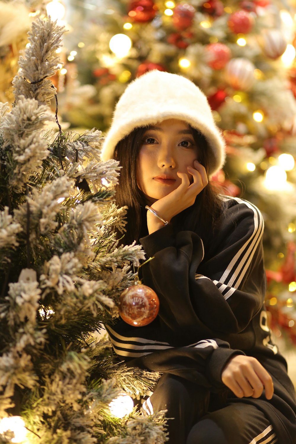 a young woman sitting on the ground next to a christmas tree