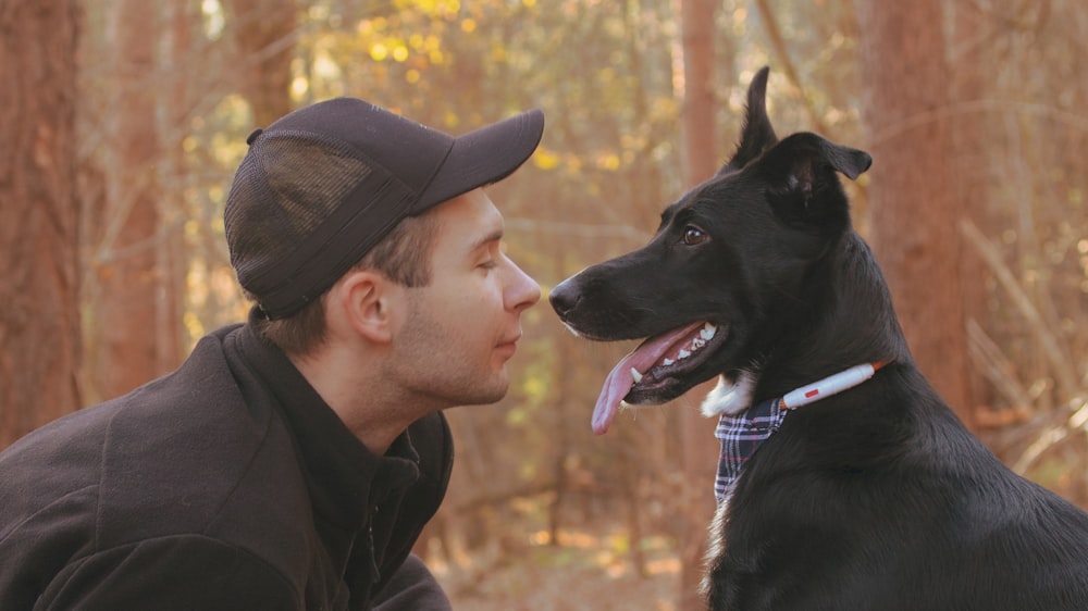 a man sitting next to a black dog in a forest