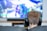 A person with short brown hair is sitting on a couch wearing black headphones. In front of them is a large screen displaying a video game with vibrant colors and dynamic visuals. The focus is on the person from behind, emphasizing the immersive gaming experience.