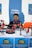 A young man is sitting and smiling at a booth with a blue backdrop that has the logo and name of Sakarya University. Various drones and related equipment are displayed on the table in front of him.
