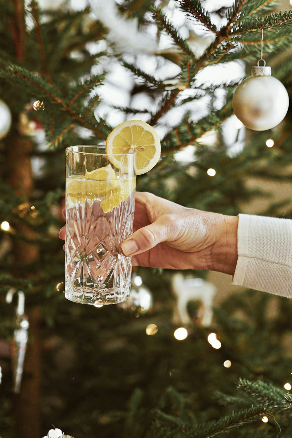 a person holding a glass of alcohol in front of a christmas tree