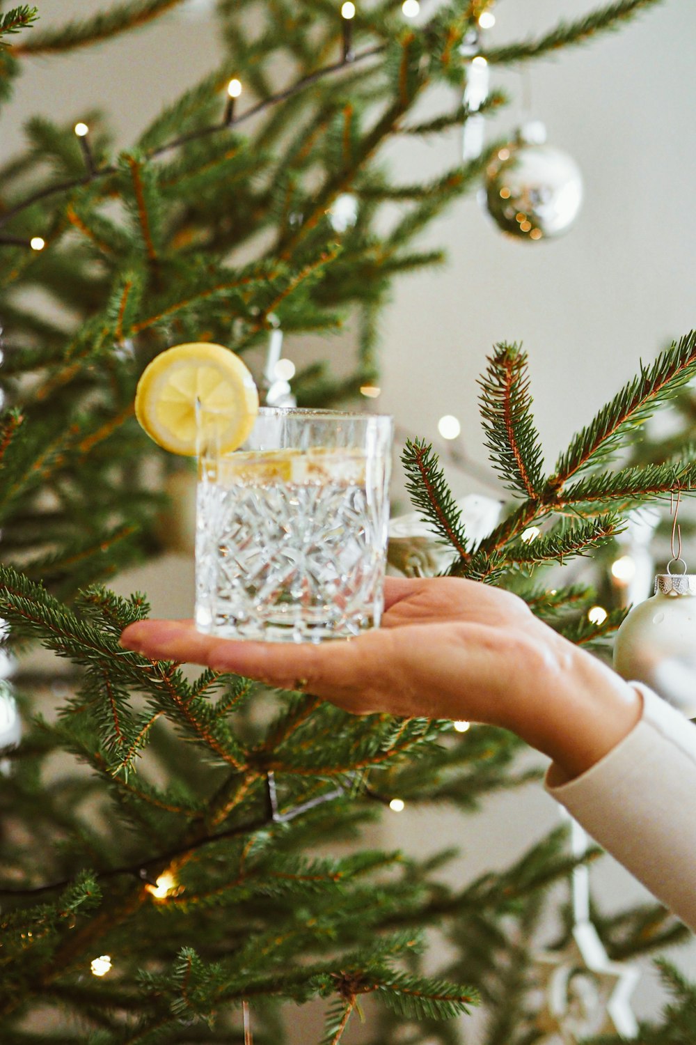 a person holding a glass in front of a christmas tree