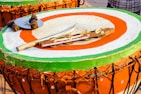 A large, round drum with a brightly painted surface featuring green, orange, and white concentric circles. Atop the drum are various percussion instruments, including sticks wrapped in fabric, a metal disc, and a wooden rod with cymbal-like attachments.