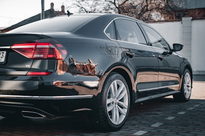 A shiny black sedan gleaming after a full mobile detail session in a sunny driveway.