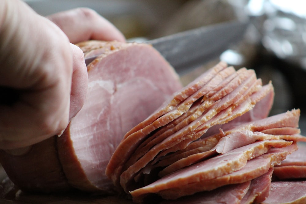 a person slicing ham on a cutting board