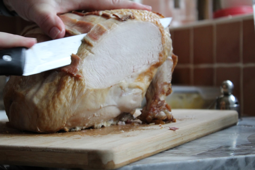 a person slicing a turkey on a cutting board,