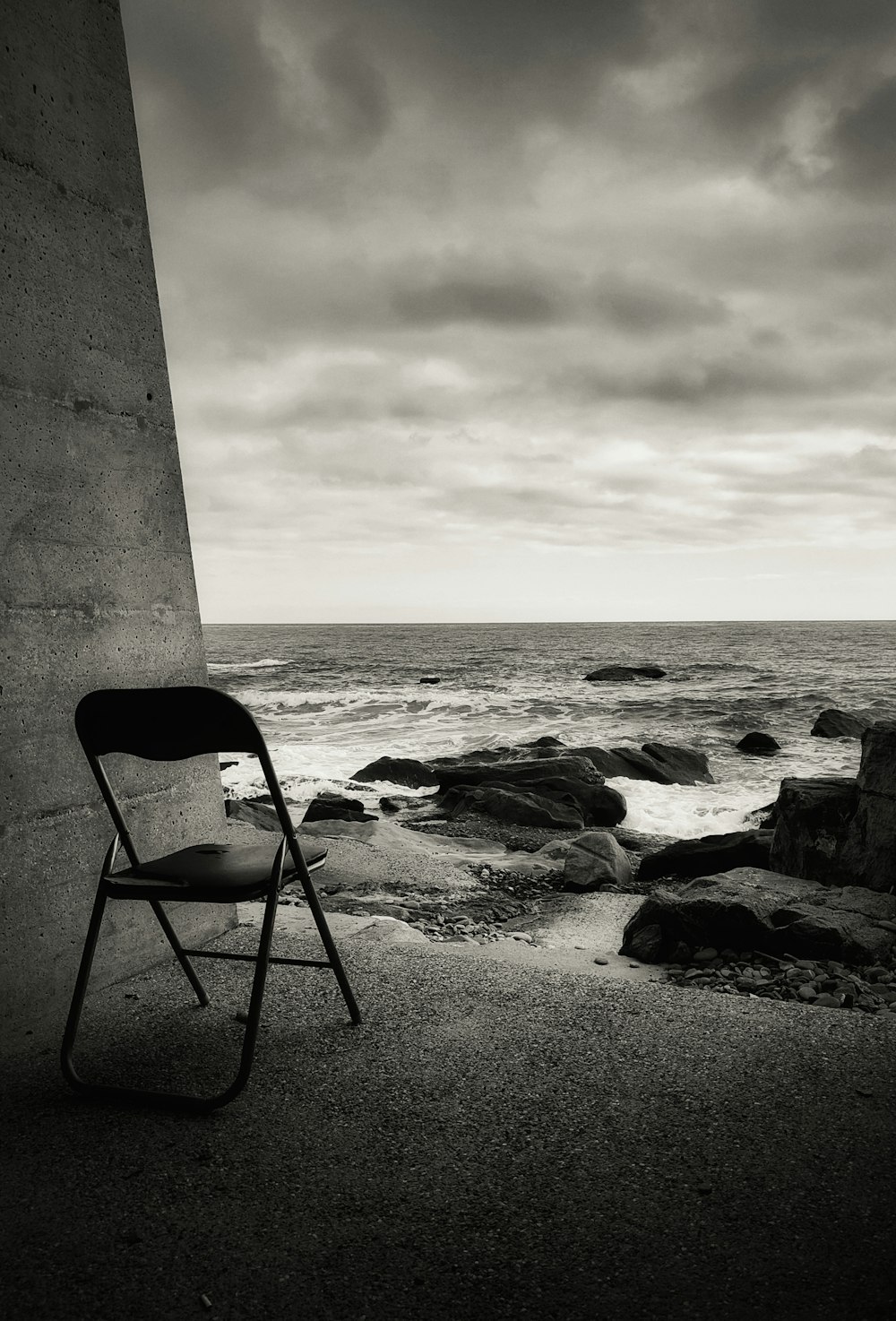 a black and white photo of a chair by the ocean