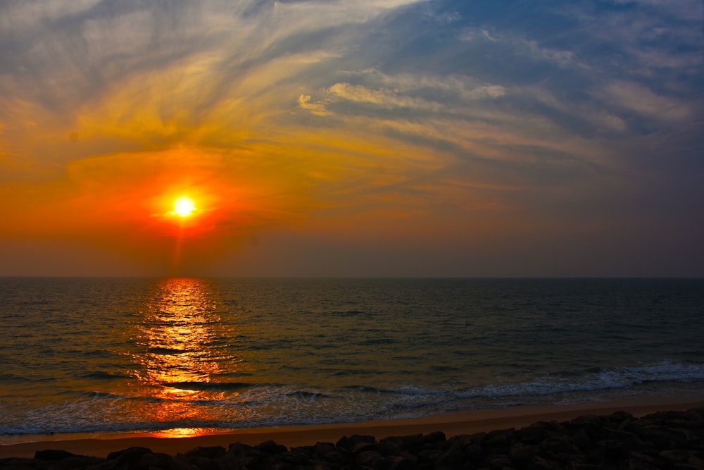 the sun is setting over the ocean on a cloudy day