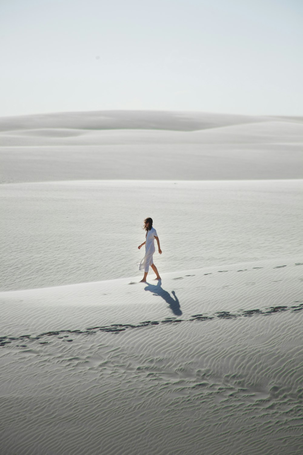 a woman in a white dress walking across a desert