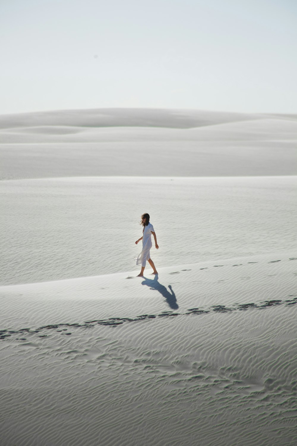 uma mulher em um vestido branco andando através de um deserto