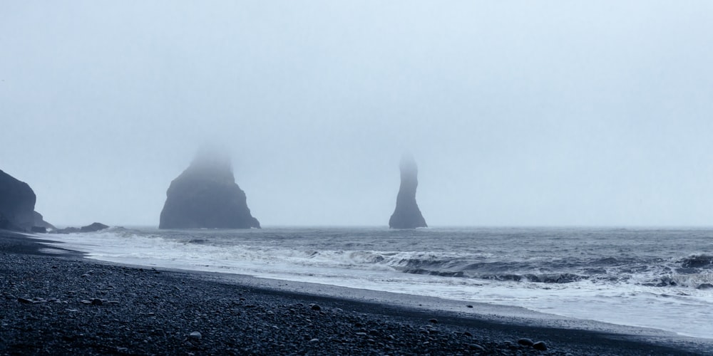 a foggy day at the beach with black rocks