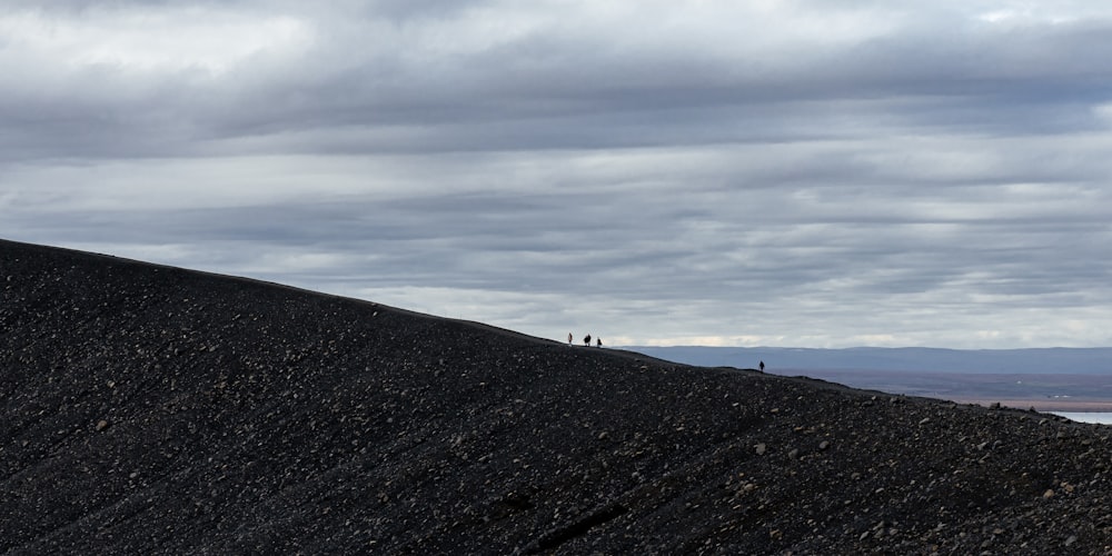 two people standing on top of a black hill