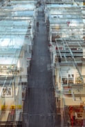 A complex, layered view of an interior space showcasing a modern art gallery or exhibition. Glass walls and partitions create a maze-like effect, with framed artworks visible on the walls. The perspective stretches into the distance, leading the eyes along a central path where a lone figure is walking.