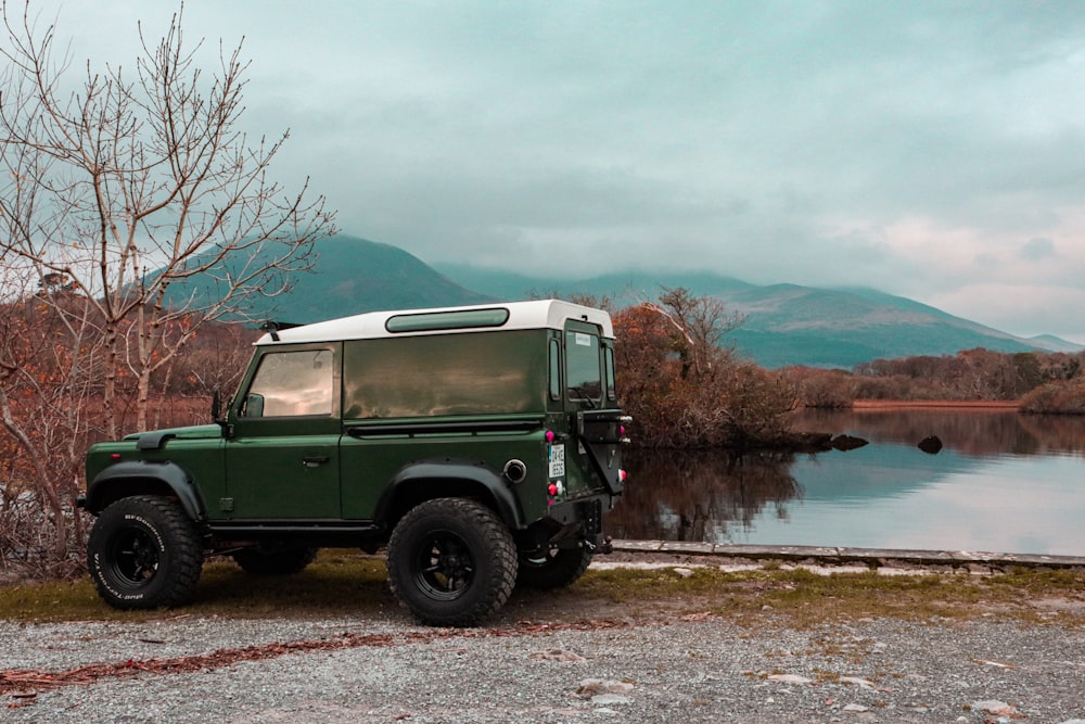 a green and white jeep parked next to a body of water