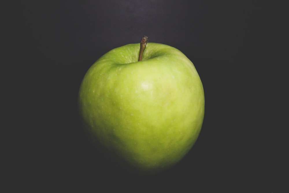 a green apple sitting on top of a black table