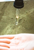 Top-down view of a hand holding a dropper releasing hair oil onto palm, with parchment texture background.