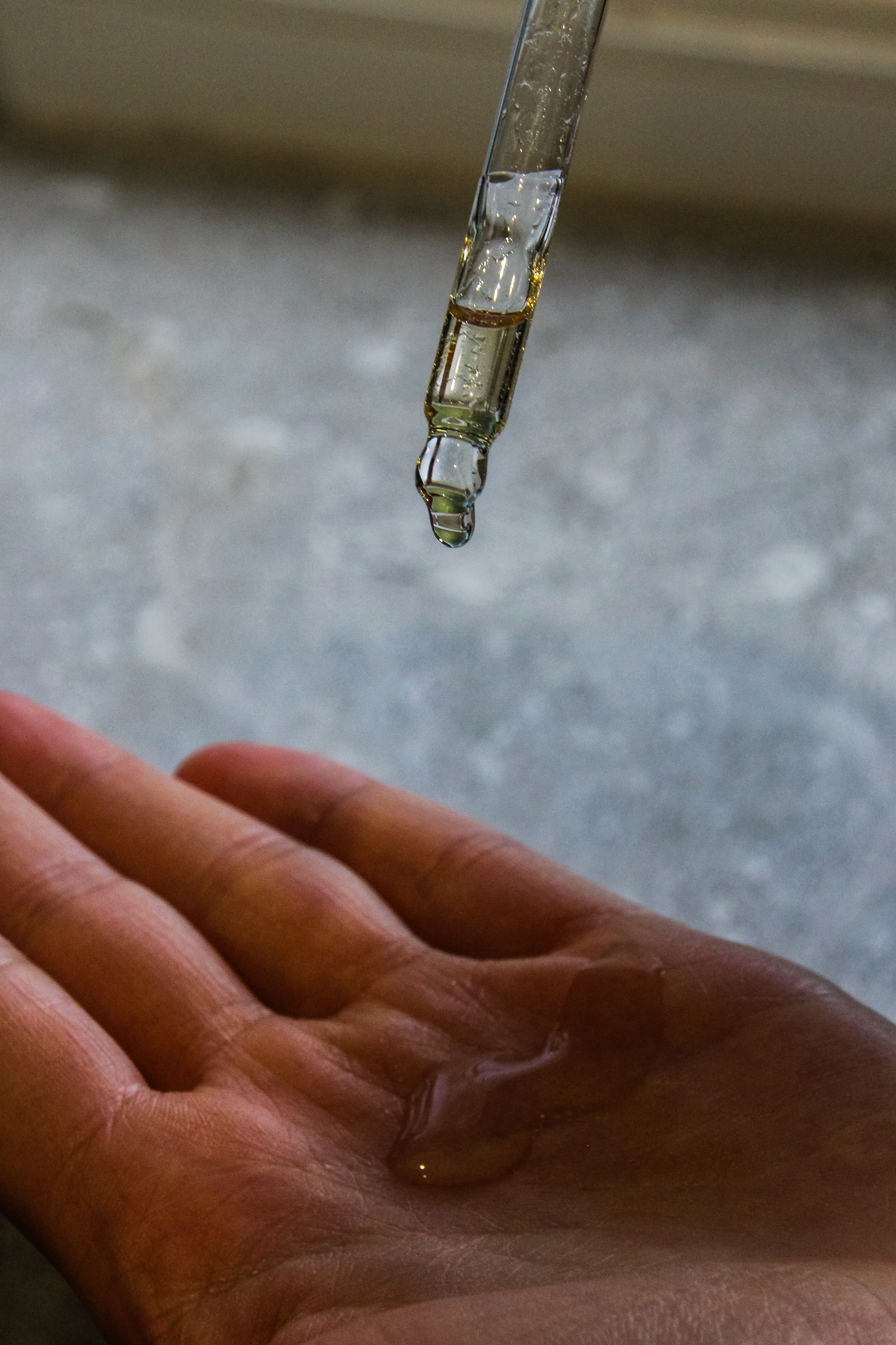 Glass dropper releasing a drop of golden oil into an open palm above a stone surface