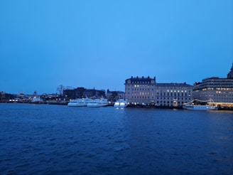 A serene waterfront view with boats and city lights reflecting on the water.