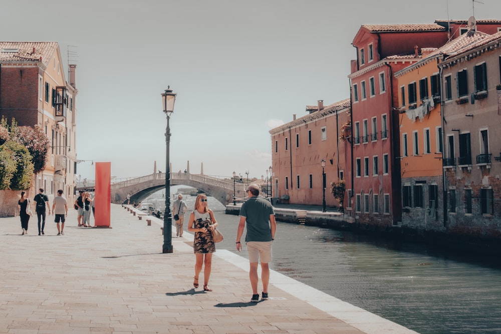 a man and a woman standing on a sidewalk next to a river