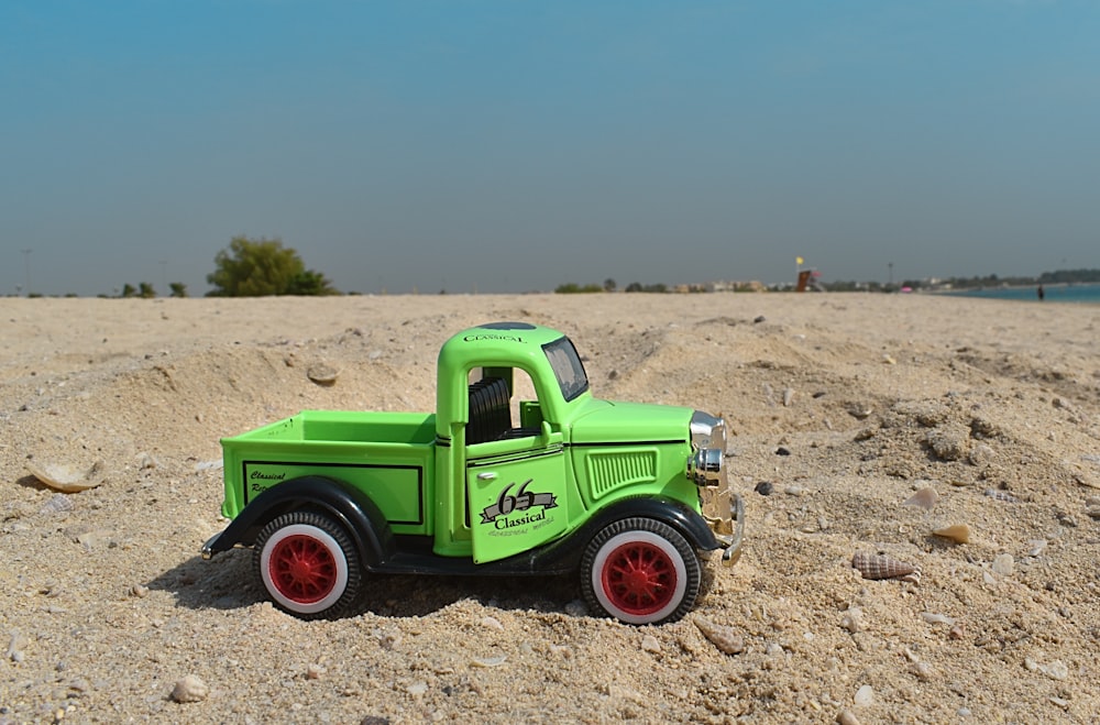 Un camión de juguete verde sentado en la parte superior de una playa de arena