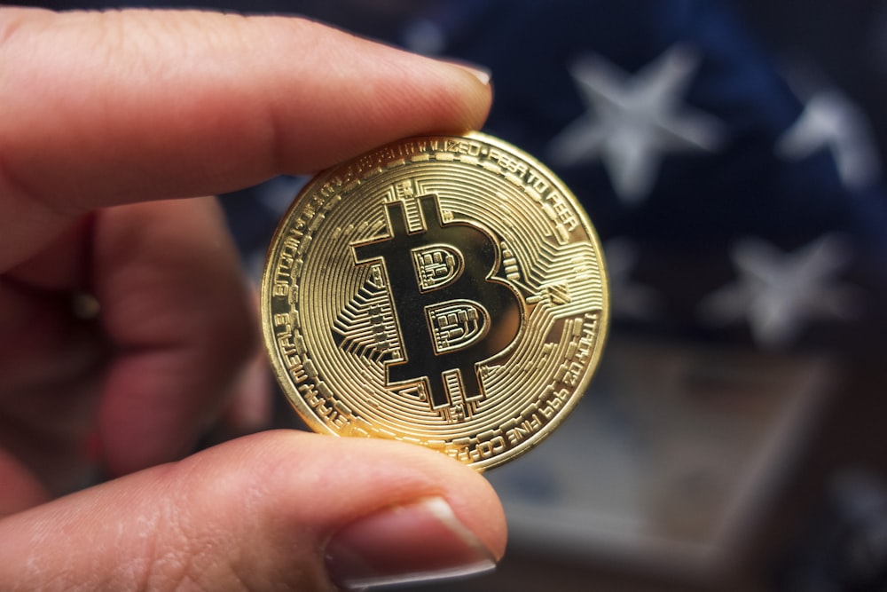 a hand holding a bit coin in front of an american flag