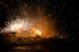 Bright sparks and a burst of orange flames create an intense and dynamic scene against a dark background. The chaos of flying embers and the contrast between light and shadow emphasize the explosive energy.