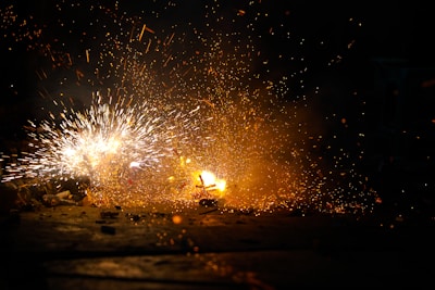 Bright sparks and a burst of orange flames create an intense and dynamic scene against a dark background. The chaos of flying embers and the contrast between light and shadow emphasize the explosive energy.