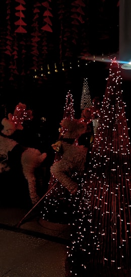 The image features festive decorations with reindeer figures covered in white and red details, surrounded by cone-shaped structures adorned with string lights. The scene is illuminated by soft, warm lighting that casts a cozy ambiance.