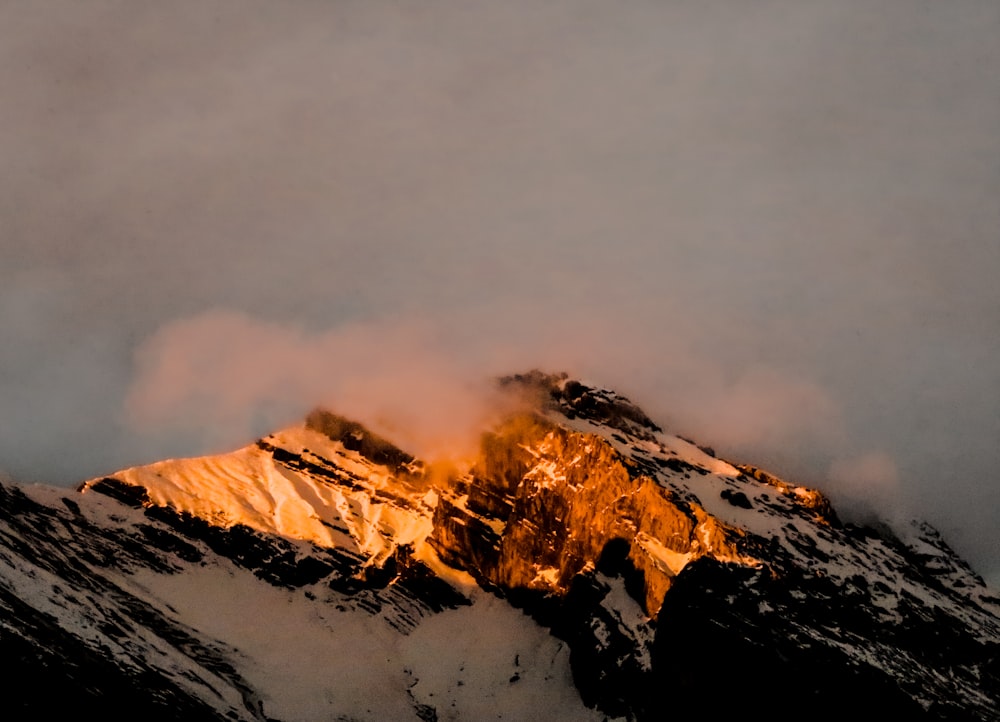 a mountain covered in snow and clouds at sunset