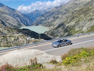 A luxury convertible cruising along the lakeside road of Lausanne with mountains in the background.