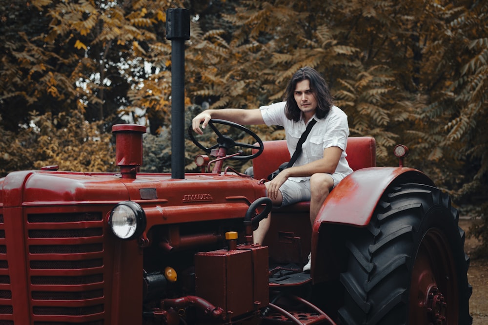 a man sitting on the front of a red tractor