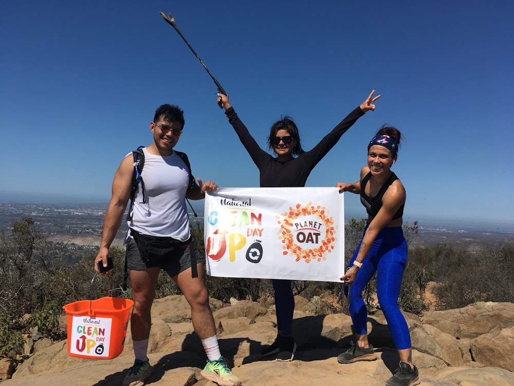 three women holding a sign on top of a mountain