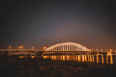 A serene starry night sky over a quiet bridge illuminated by soft celestial light.