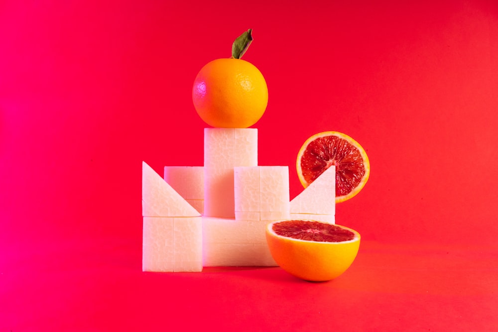 Una naranja sentada encima de un bloque de queso junto a un pomelo