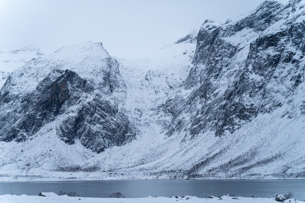 a mountain covered in snow next to a lake