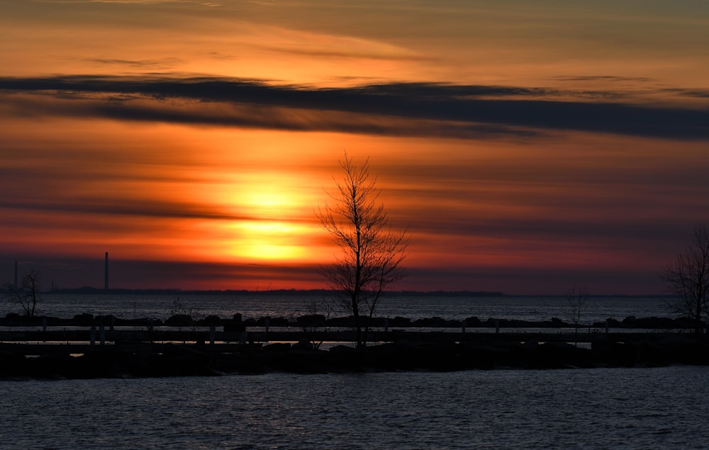 a sunset over a body of water with trees in the foreground