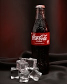 a bottle of coca cola sitting on top of ice cubes