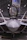 A sleek, modern fighter jet with a sharp, aerodynamic design is positioned inside a spacious hangar. The cockpit canopy is open, revealing part of the interior. Overhead lighting casts a soft glow on the aircraft's smooth surface, highlighting its stealthy angles and engineering.