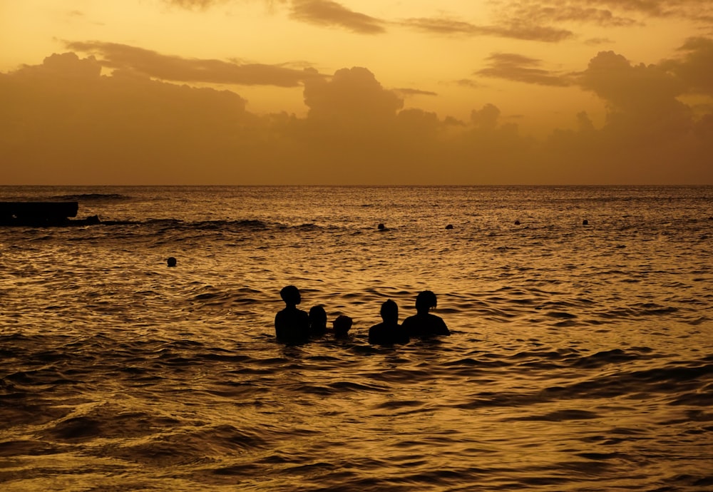 a group of people swimming in the ocean at sunset