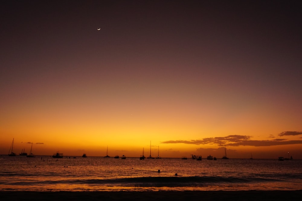 a sunset over the ocean with sailboats in the distance